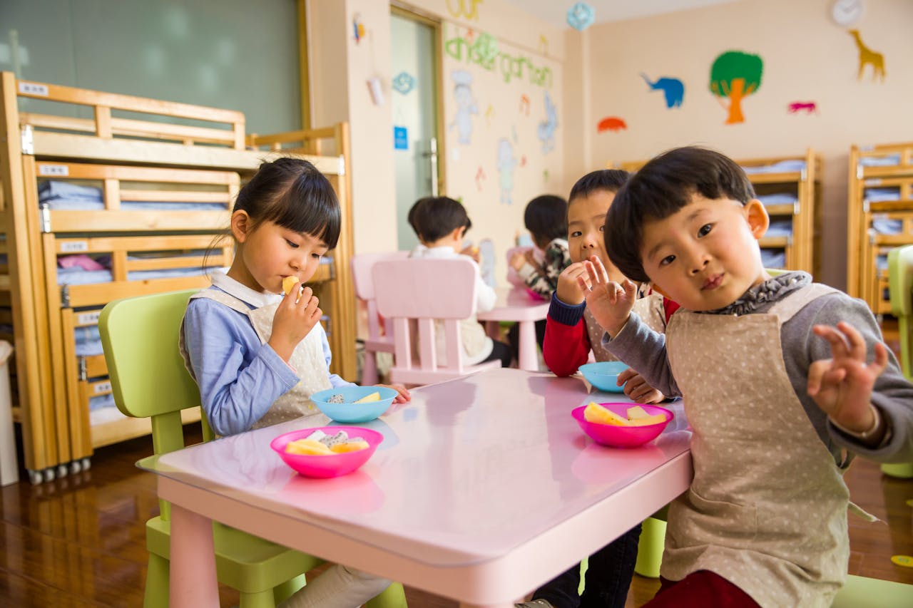 about-02 Kids seated around a table in a colorful classroom, eating snacks happily.