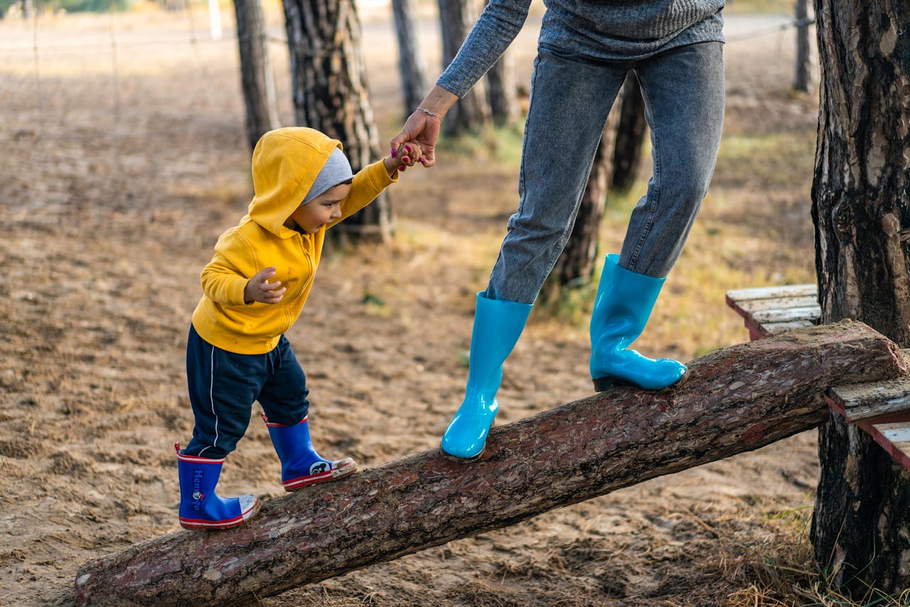 about-04 A woman helps her toddler walk on a log in a park, showcasing child support and family bonding.